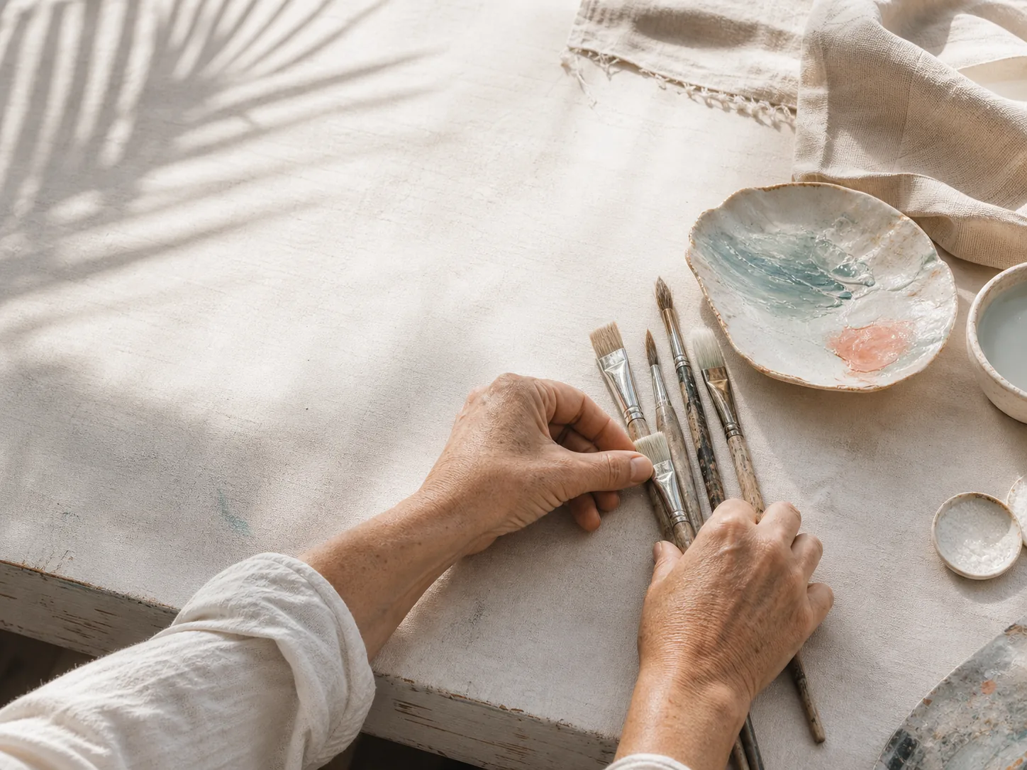 Concept study of an artist's hands arranging paintbrushes on a sunlit work table